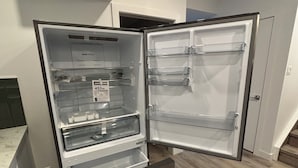 Een open koelkast met meerdere planken en een vriesvak, geplaatst in een keuken met houten vloeren en witte kasten.