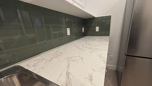 Een keuken met een marmeren aanrechtblad, groene spatwand, een roestvrijstalen spoelbak en een geïntegreerde koelkast.
