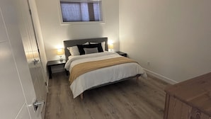 Een slaapkamer met een bed, nachtkastjes, een raam en een houten vloer.