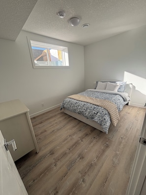A bedroom with a bed, a window, a desk, and a ceiling with three light fixtures.