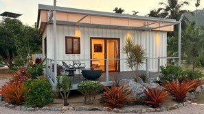 A modern house with a covered porch, a large black planter, and tropical plants. - This Great Place (Don Sak)