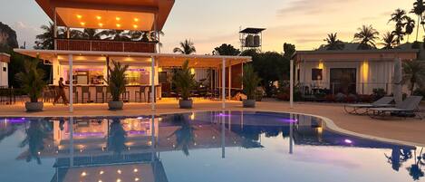 A resort with a swimming pool, outdoor bar, and lounge area.