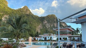 A resort with a pool, palm trees, and a mountain backdrop. - This Great Place (Don Sak)