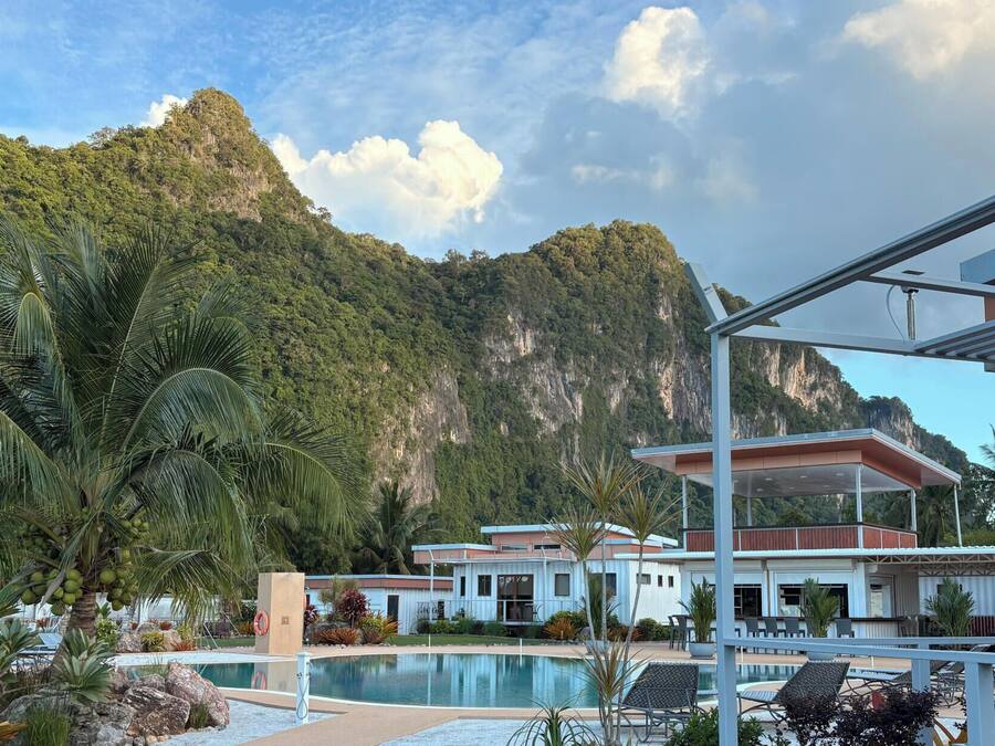 Un resort con piscina, palmeras y montañas al fondo.