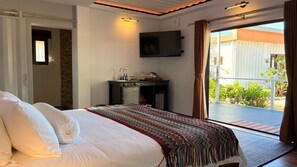Een hotelkamer met een bed, een bureau met een flatscreen televisie, een balkon met uitzicht op groen en een schuifdeur.