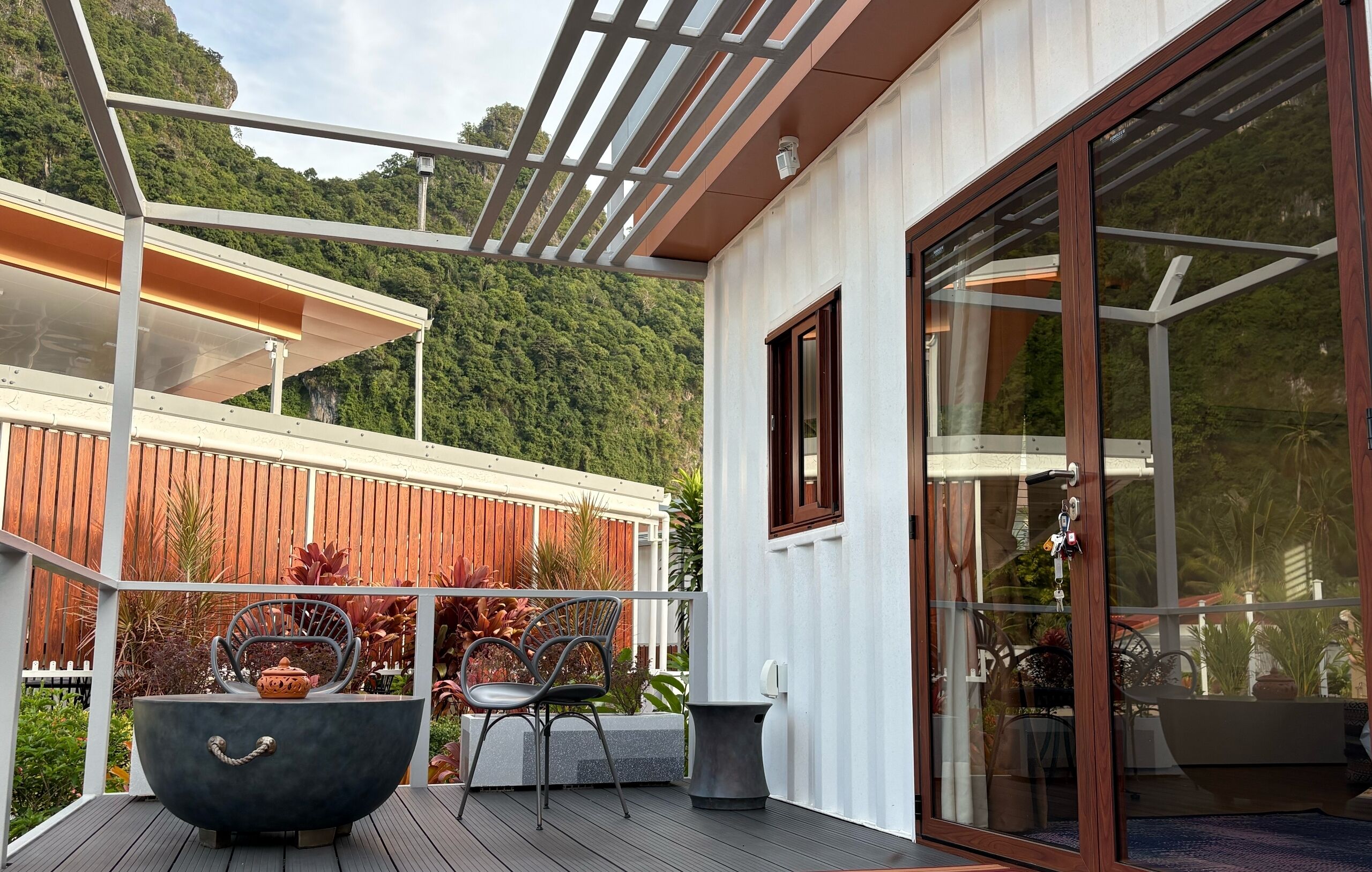 A modern outdoor deck with a glass door, metal railing, and a view of a forested hillside.