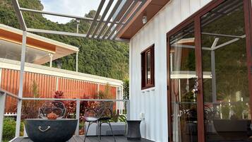 A modern outdoor deck with a glass door, metal railing, and a view of a forested hillside.