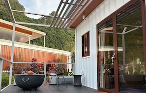 A modern outdoor deck with a glass door, metal railing, and a view of a forested hillside.