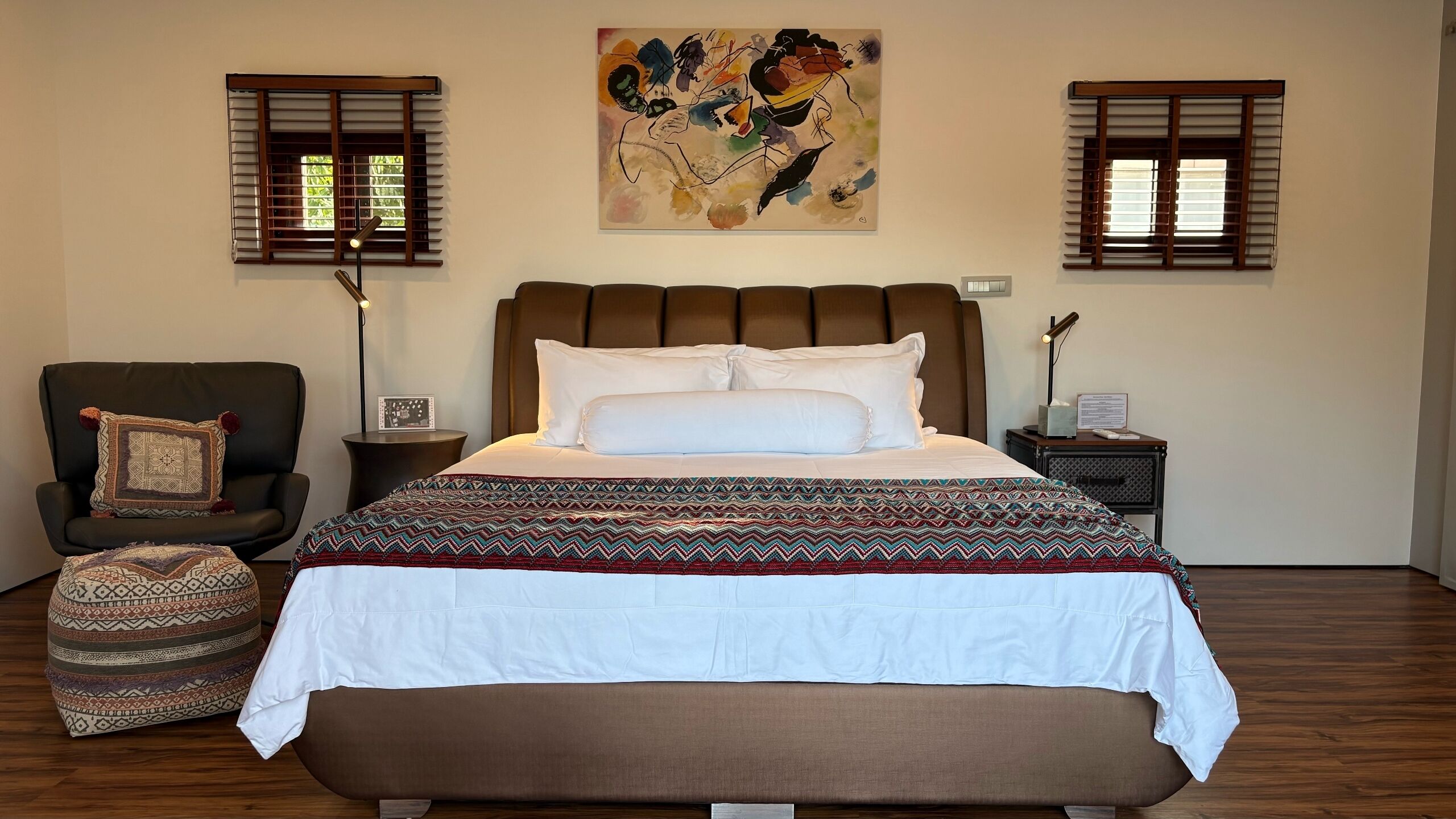 Un dormitorio con una cama grande, una silla, una mesita de noche y una obra de arte en la pared.