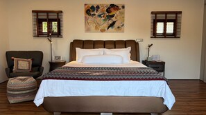 A bedroom with a large bed, a chair, a bedside table, and a wall-mounted artwork. - This Great Place (Don Sak)