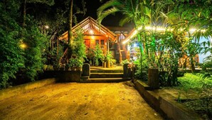 A wooden house with a porch and steps leading to the entrance, surrounded by lush greenery and potted plants. - Shan Homestay (Sigiriya,)