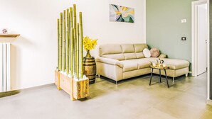 Uma sala de estar com sofá, uma mesinha, uma planta de bambu decorativa e um quadro na parede.