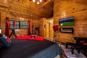 Un dormitorio de cabaña de madera con una cama, televisor montado y chimenea.