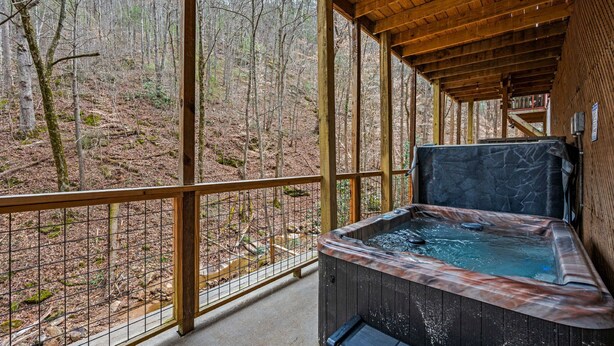 A wooden deck with a hot tub overlooking a forested area. - NEW Kink Cabin w/ Private Creek (Sevierville)