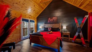 A wooden cabin bedroom with a bed, a nightstand, a lamp, and a red blanket. - NEW Kink Cabin w/ Private Creek (Sevierville)
