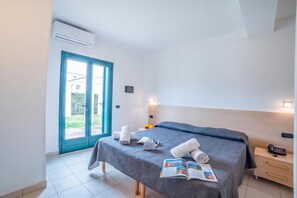 Ein Hotelzimmer mit Bett, Nachttisch, Lampe, Fenster mit Aussicht und einer Klimaanlage.