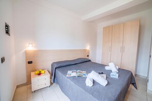 Ein Hotelzimmer mit einem Bett, einem Nachttisch, einem Schrank und einem kleinen Tisch mit Zeitschrift und Handtüchern.