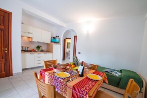 Ein Essbereich mit Tisch für zwei Personen, eine Küche im Hintergrund und ein grünes Sofa.