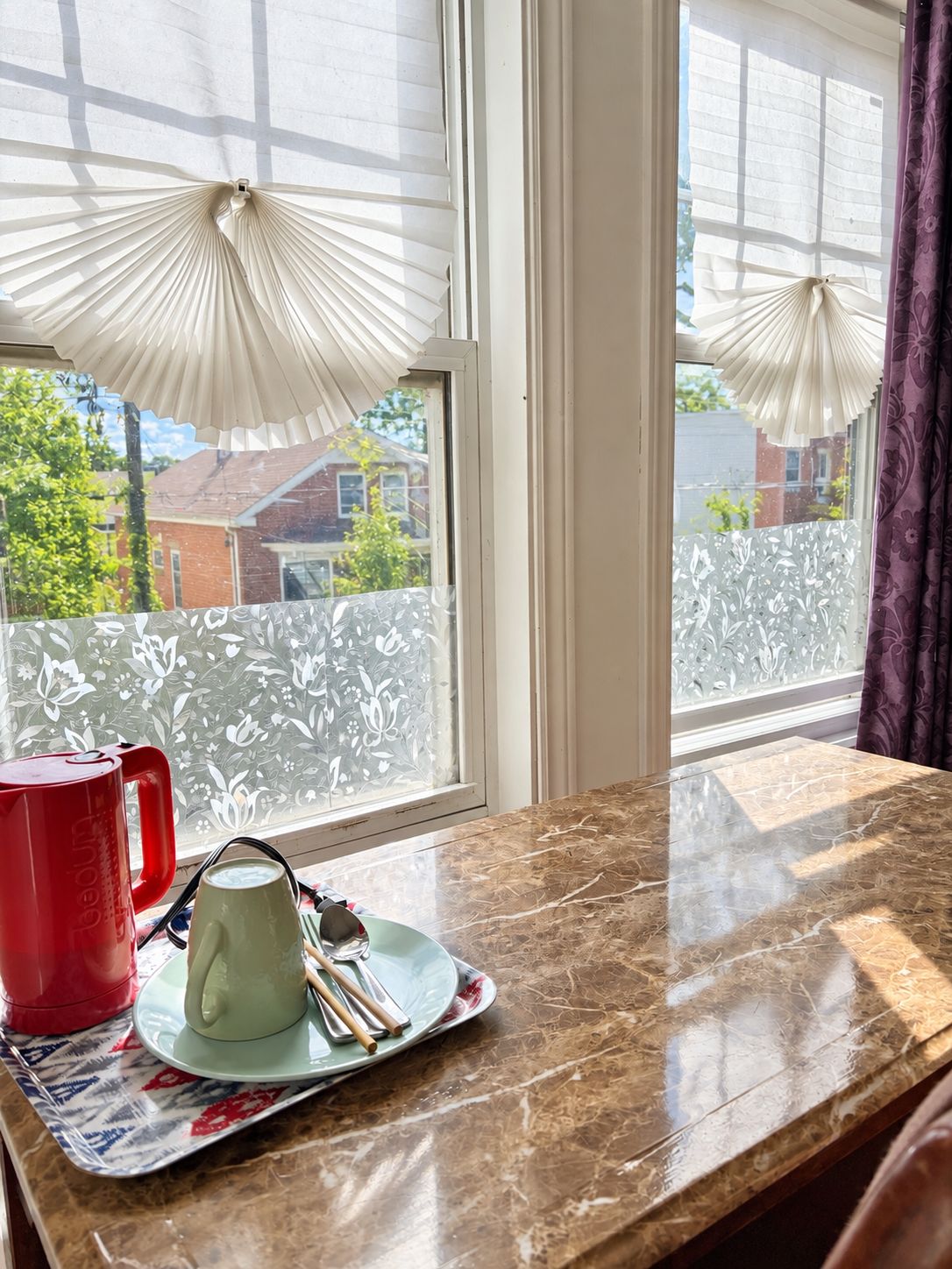 A room with a marble countertop, a red mug, a green mug, and a plate with utensils.