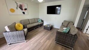 Ett vardagsrum med en soffa, två fåtöljer, ett soffbord, en platt-TV och en takfläkt.