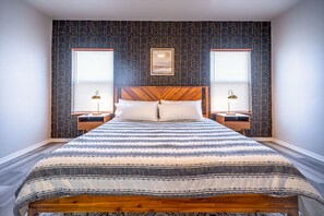 A bed with a striped blanket, two bedside lamps, and a headboard with a picture above it. - The Mohave Modern: a 3bed/2bath Cozy, Central Desert Retreat (Kingman)