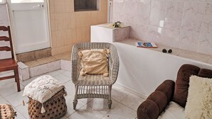 Ein Badezimmer mit einer Badewanne, einem Korbstuhl, einem braunen Sofa und einem kleinen Hocker.