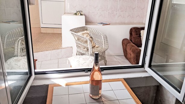 Ein Zimmer mit einem weißen Korbstuhl, einem braunen Sofa, einer weißen Kommode und einer Flasche auf einem Tisch.