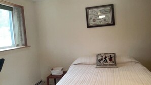 A bedroom with a bed, a framed map on the wall, a small table with a bowl, and a window with curtains.