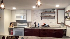A kitchen with white cabinets, a microwave, a stove, a sink, and a marble countertop.