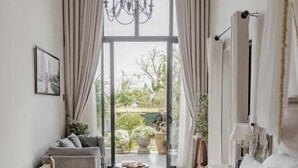 A bedroom with a large bed, a chandelier, curtains, a sofa, and a view of the outdoors.