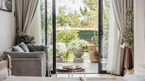 A room with a sofa, a small round table, and a view of an outdoor garden through a glass door.