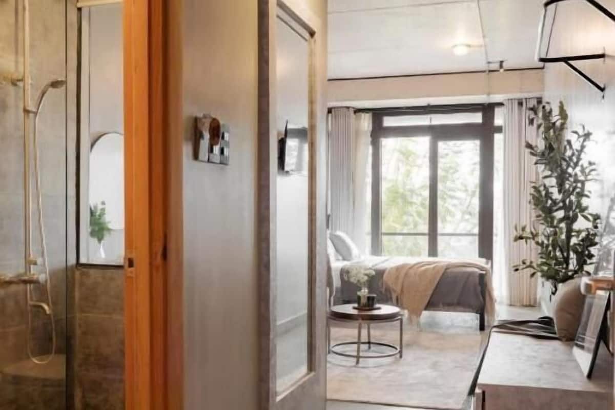 A modern hotel room with a shower, a bed, a desk, and a large window.