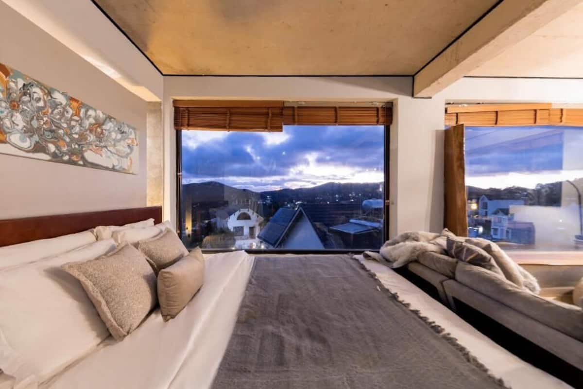 A bedroom with a large window, a bed, a sofa, and a painting on the wall.