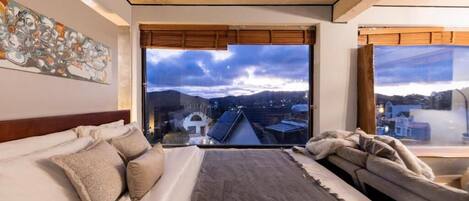 A bedroom with a large window, a bed, a sofa, and a painting on the wall.