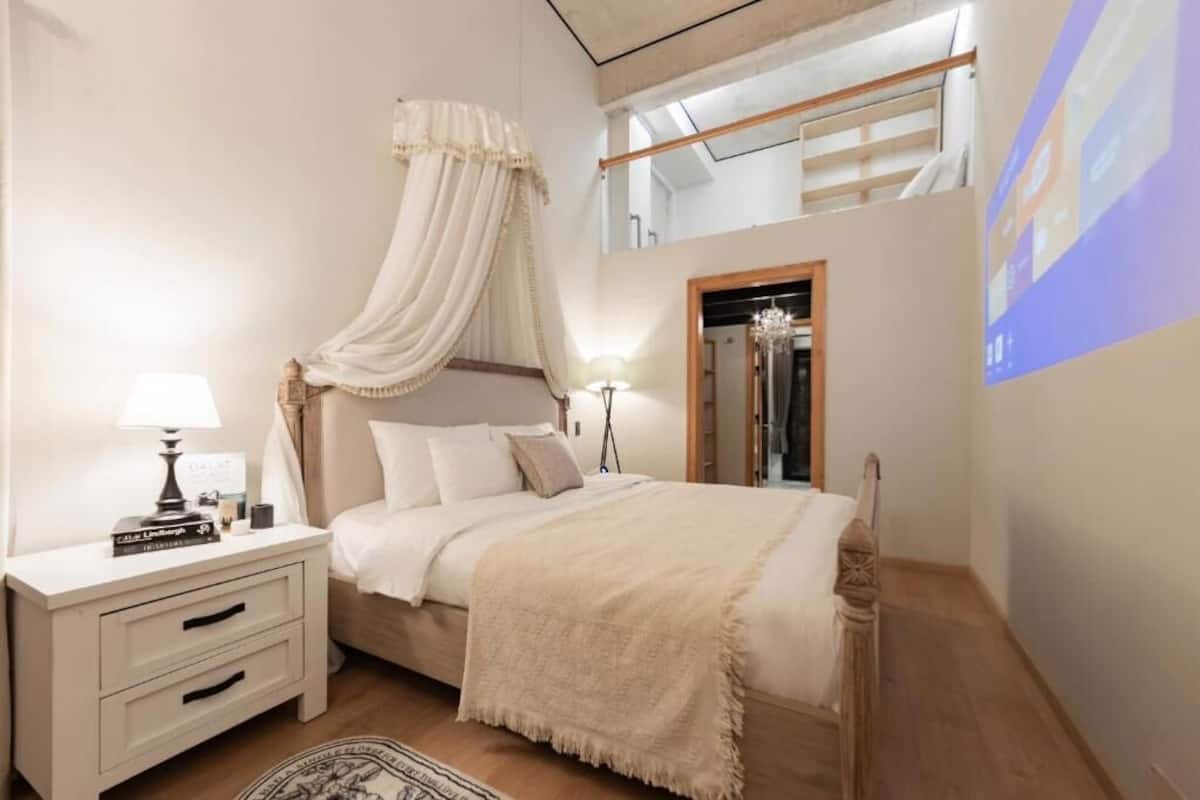A bedroom with a canopy bed, bedside table, lamp, and a mirror.