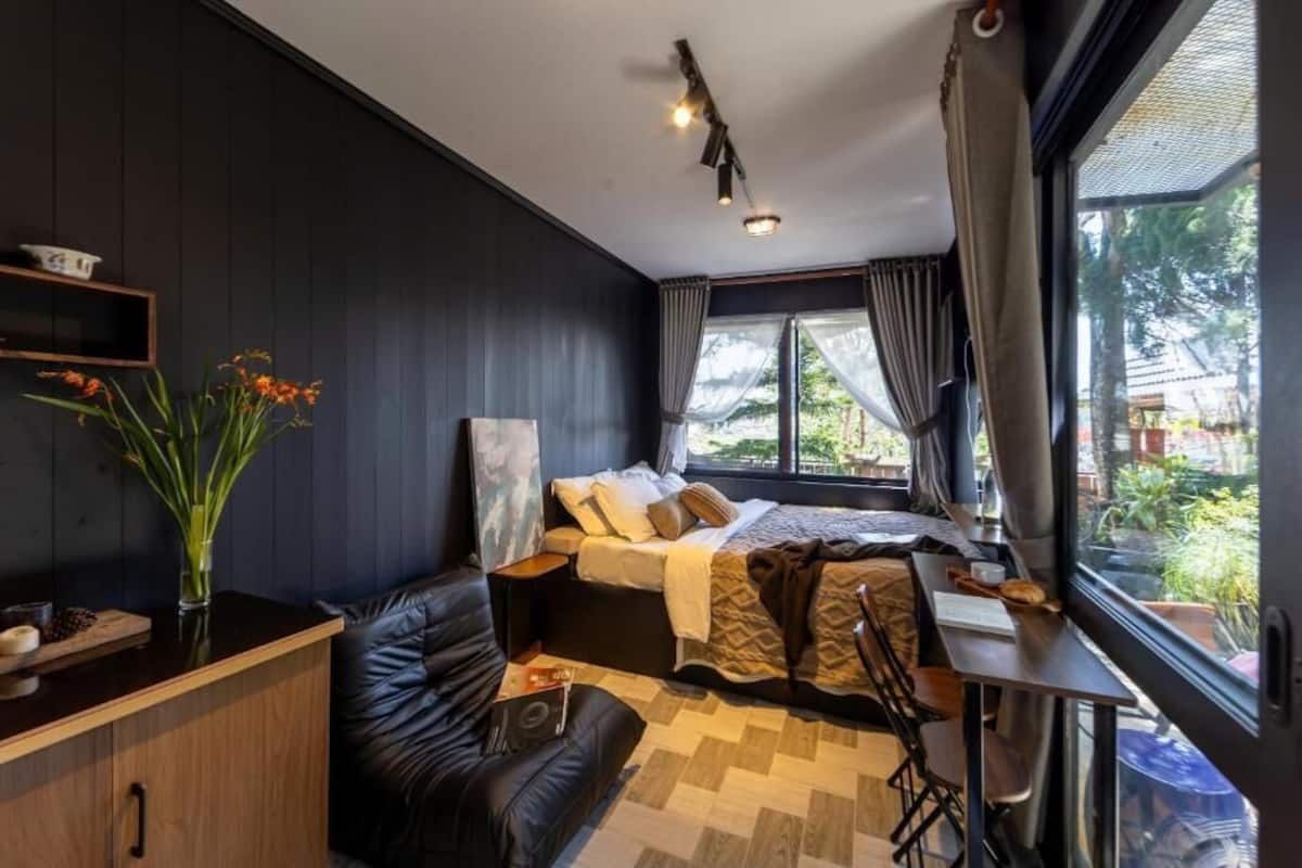 A compact room with a bed, a desk, a chair, a sofa, and a window with curtains.