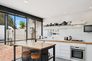 Une cuisine moderne dotée d’une grande fenêtre, d’une table en bois, de tabourets de bar, de meubles blancs et d’un four encastré.