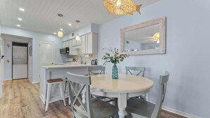 A dining area with a round table, chairs, a vase, and a mirror on the wall. - Beachfront 2BR Condo with Pool and Beach Access (Gulf Shores)