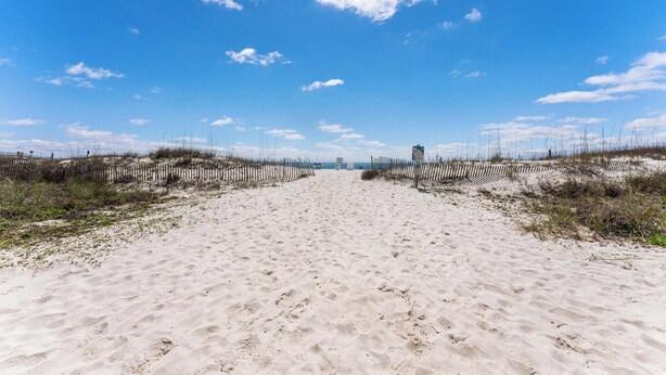 A sandy beach path with a fence on both sides, leading to a distant structure. - Beachfront 2BR Condo with Pool and Beach Access (Gulf Shores)