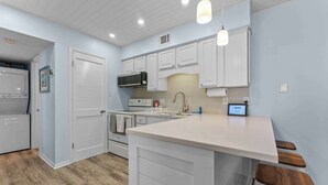 A kitchen with white cabinets, a white countertop, and wooden stools. - Beachfront 2BR Condo with Pool and Beach Access (Gulf Shores)