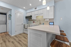 A kitchen with white cabinets, a white countertop, and wooden stools. - Beachfront 2BR Condo with Pool and Beach Access (Gulf Shores)