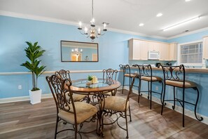 A dining area with a round table, chairs, a chandelier, a potted plant, and a kitchen in the background. - Ground Floor 2BR Near Golf & Beach (Myrtle Beach)