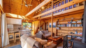 A cozy cabin interior with a living area, kitchen, and bookshelves.