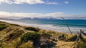 A beach with a wooden deck, chairs, and a view of the ocean and distant mountains.