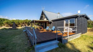 A cabin with a deck, outdoor seating, and a stone structure in the background.