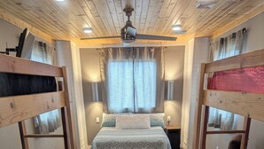 A bunk bed room with a wooden floor, a central bed with a patterned bedspread, and a ceiling fan.