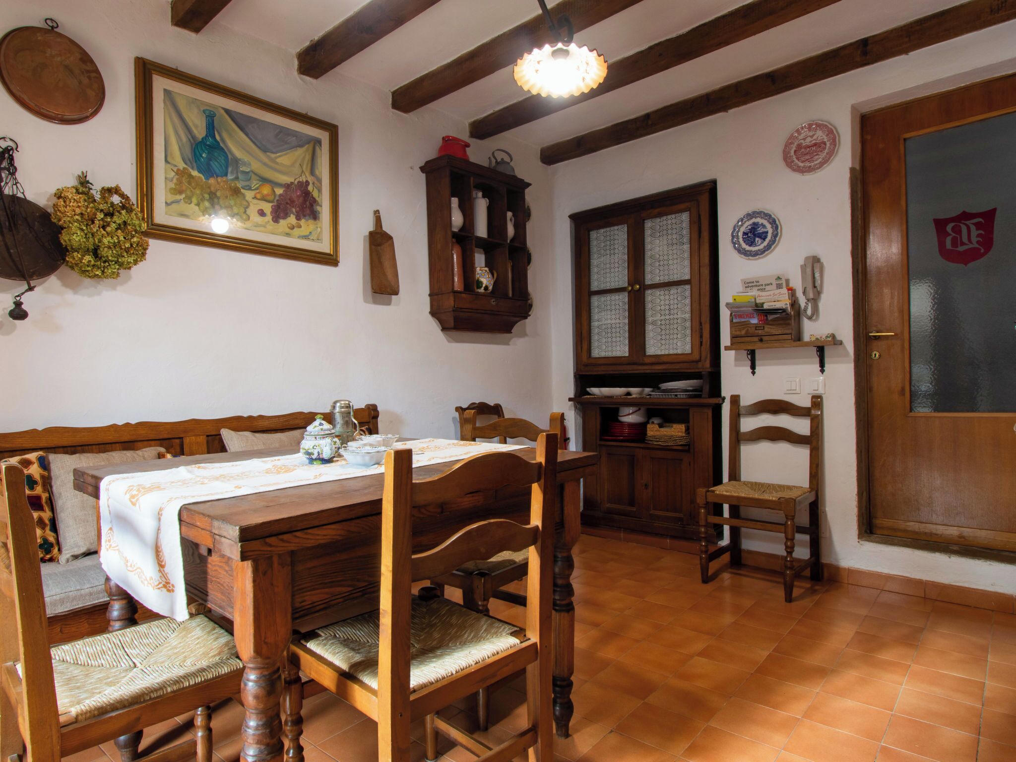 A dining area with a wooden table and chairs, a cabinet with glass doors, and a painting on the wall.