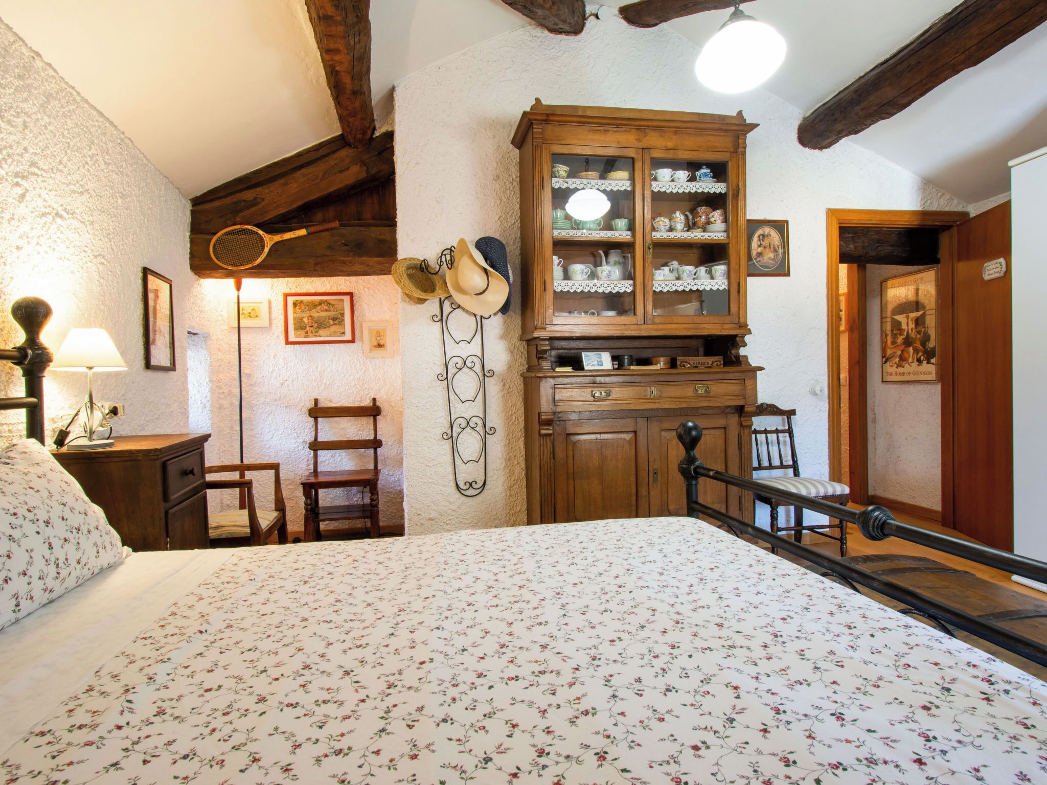Een slaapkamer met een bed, houten meubels, een kast met glazen deuren en een plafond met zichtbare balken.