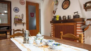 A dining table with a white tablecloth, a coffee pot, cups, and bowls. There are chairs around the table, a wooden cabinet with kitchen utensils, and a door with a coat of arms. - Apartment Torre by Interhome (Palazzuolo Sul Senio)