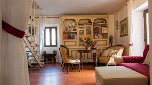 A traditional room with a staircase, a wooden table with chairs, a sofa, and a bookshelf filled with books and decorative items. - Apartment Torre by Interhome (Palazzuolo Sul Senio)